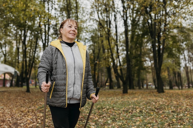 Anciana sonriente con bastones de trekking al aire libre y espacio de copia