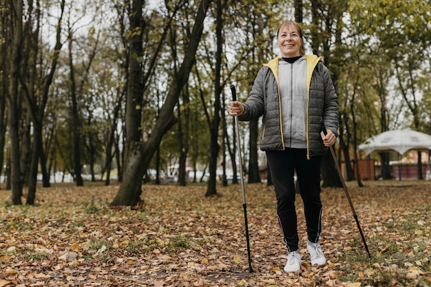 Anciana sonriente con bastones de trekking y espacio de copia