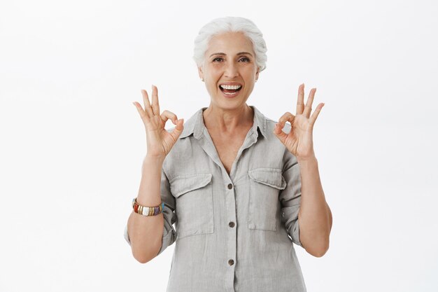 Anciana sonriente complacida que muestra un gesto bien en aprobación, recomienda compañía, como idea