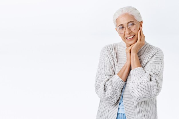 Anciana sonriente, feliz mujer mayor con gafas con cabello gris, mirando cámara encantada y alegre, sonriendo mientras toca la cara y contempla a su nieto jugando