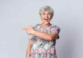 Foto gratuita anciana sorprendida apunta al lado mirando aislado en la pared blanca