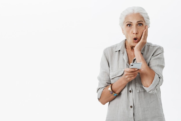 Anciana sorprendida y asombrada mirando y sosteniendo el teléfono inteligente