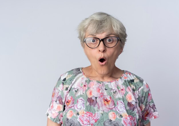 Anciana sorprendida en gafas ópticas se ve aislado en la pared blanca