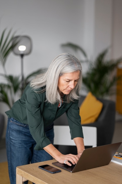 Anciana de tiro medio trabajando en una computadora portátil en casa