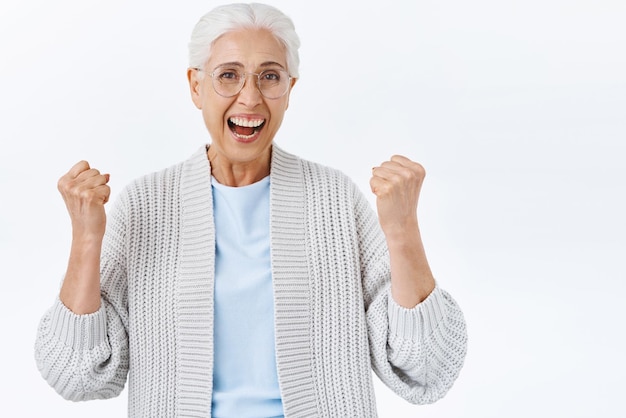 Foto gratuita la anciana triunfante ve la televisión cuando escuchó que ganó la lotería levantando las manos con satisfacción y sonriendo alegremente convirtiéndose en campeona ganó un premio increíble y celebrando la victoria fondo blanco