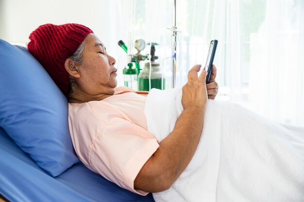 Anciana utiliza smartphone en la cama del paciente en el hospital