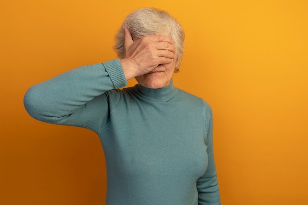 Anciana vistiendo suéter de cuello alto azul que cubre los ojos con la mano