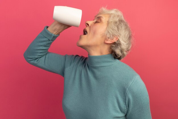 Anciana vistiendo suéter de cuello alto azul sosteniendo una taza de té