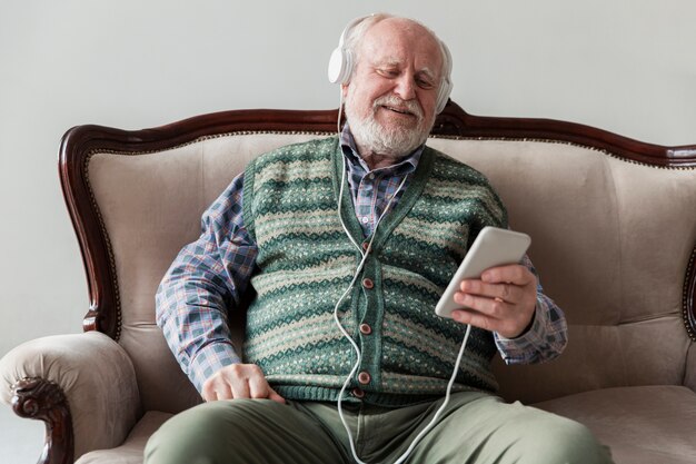 Anciano de alto ángulo en el sofá tocando música en el móvil