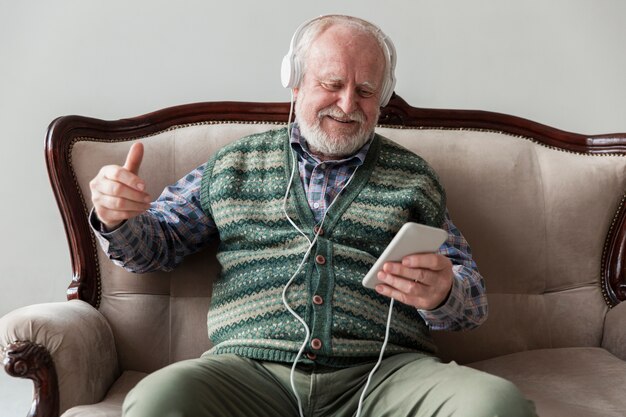 Anciano de alto ángulo en el sofá tocando música en el teléfono