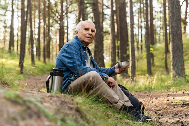 Anciano descansando mientras viaja con mochila en la naturaleza