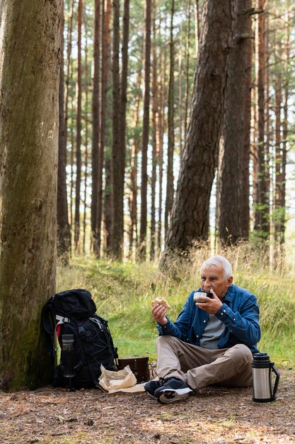 Anciano descansando en la naturaleza mientras viaja con mochila