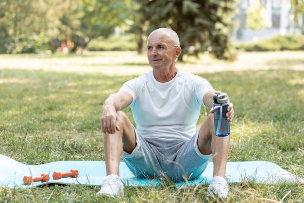 Anciano descansando sobre estera de yoga al aire libre