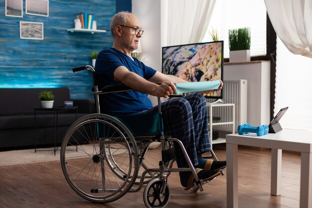Anciano discapacitado en la resistencia del brazo de entrenamiento en silla de ruedas que ejercita los músculos del cuerpo