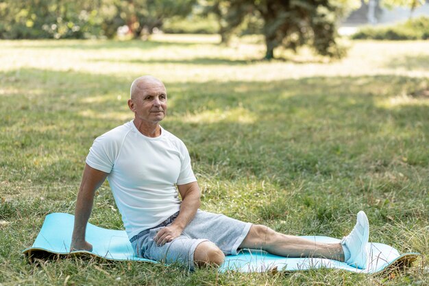 Anciano estirando sobre estera de yoga en la naturaleza