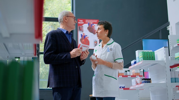 Foto gratuita anciano en farmacia pidiendo opinión médica al farmacéutico, necesitando tratamiento para la prevención del paro cardíaco. farmacéutico que ayuda a un viejo comprador a elegir el mejor medicamento para los problemas cardíacos