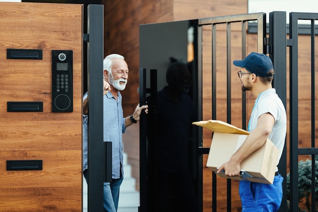 Un anciano feliz comunicándose con un mensajero que está entregando paquetes a su casa