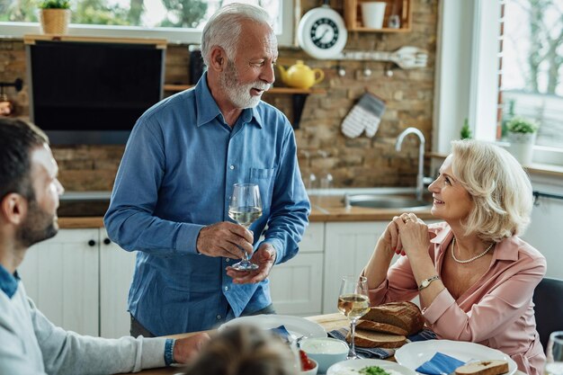 Un anciano feliz proponiendo un brindis mientras almorzaba con su familia en el comedor