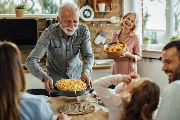 Un anciano feliz sirviendo comida en la mesa del comedor mientras almuerza en familia en casa