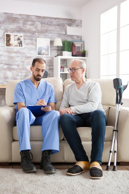 Foto gratuita anciano en hogar de ancianos hablando con médico masculino con portapapeles.