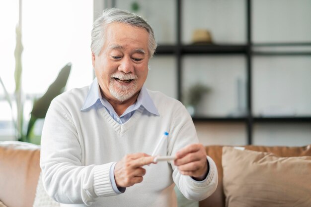 Anciano jubilado, hombre asiático, gesto de asimiento de la mano y muestra el resultado del kit de prueba rápida covid19 con signo negativo con felicidad y prueba rápida de prueba alegre en casa