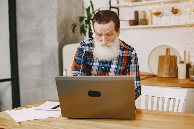 Anciano con laptop. Abuelo sentado en una decoración navideña. Hombre con camisa de celda.