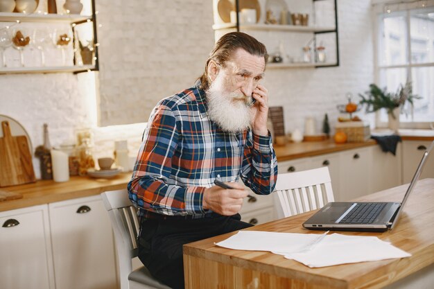 Anciano con laptop. Abuelo sentado en una decoración navideña. Hombre con teléfono móvil.