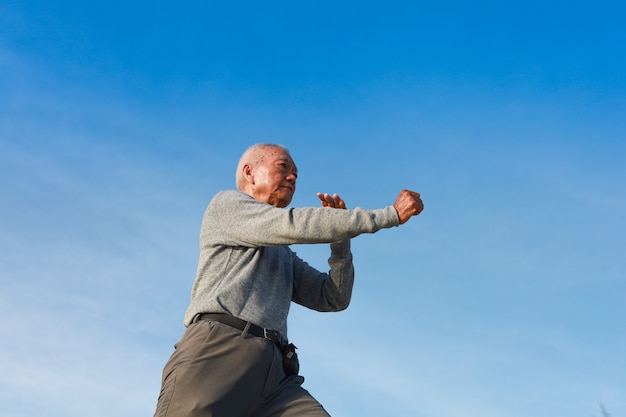 Anciano mayor asiático practicar taichi kungfu chino en la playa