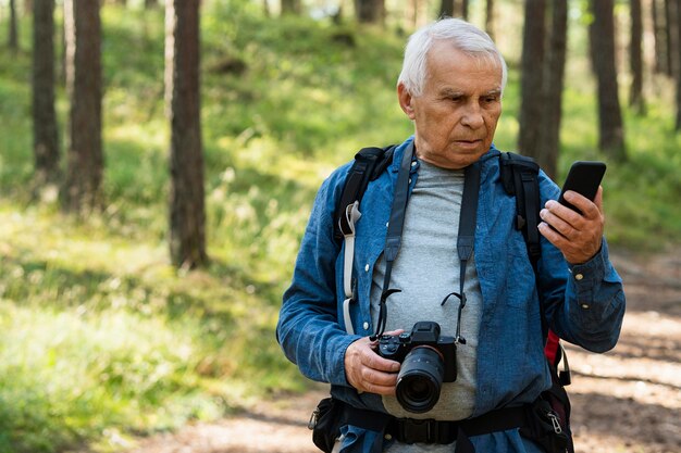 Anciano mirando smartphone mientras viaja con mochila en la naturaleza