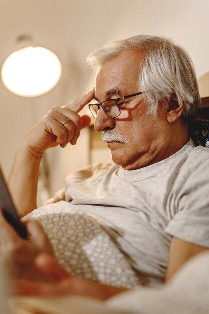 Un anciano pensativo leyendo un libro mientras se relaja en el dormitorio