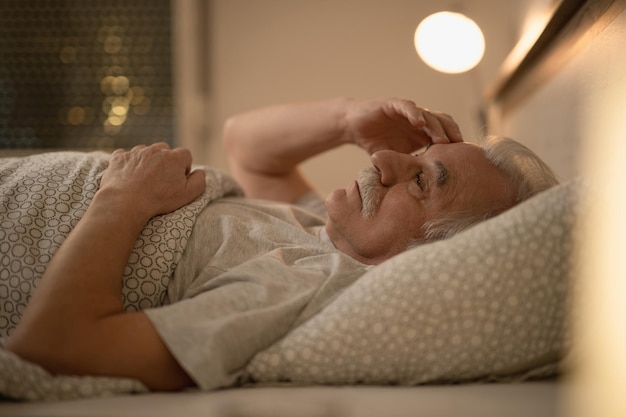 Un anciano preocupado pensando en algo mientras descansa en la cama por la noche
