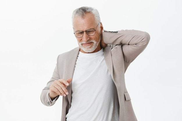 Anciano preocupado en traje quejándose de dolor de espalda, tocando el cuello