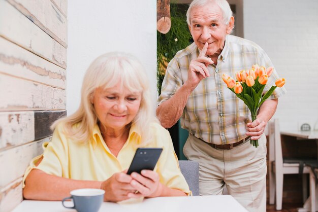 Anciano preparando sorpresa con bouquet para esposa