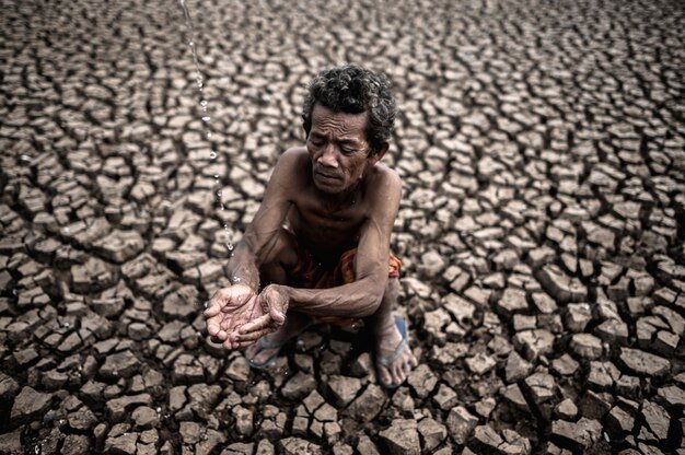 Un anciano sentado en contacto con la lluvia en la estación seca, el calentamiento global, el enfoque de selección