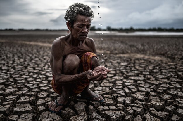 Un anciano sentado en contacto con la lluvia en la estación seca, el calentamiento global, el enfoque de selección