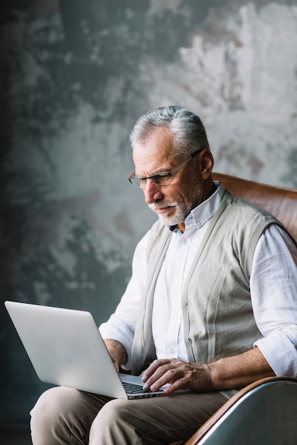 Un anciano sentado en silla escribiendo en computadora portátil