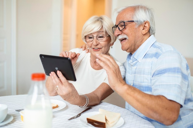 El anciano y su esposa están usando una tableta digital y comunicándose con sus hijos Una feliz pareja de ancianos está desayunando y teniendo una conversación en línea con su familia y enviando saludos
