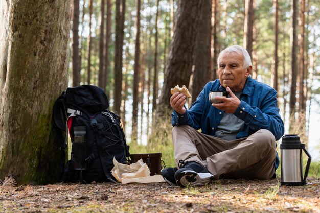 Anciano tomando una copa mientras viaja con mochila en la naturaleza