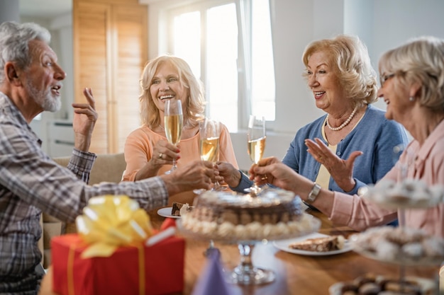 Ancianos felices divirtiéndose mientras brindan con champán y se comunican en la fiesta de cumpleaños en casa