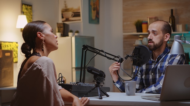 Anfitrión e invitado hablando durante un podcast con micrófono en un estudio en casa. Espectáculo creativo en línea Producción al aire, presentador de transmisión por Internet, transmisión de contenido en vivo, grabación de comunicación digital en redes sociales