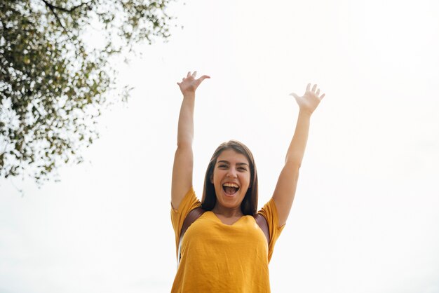 Angulo contrapicado de mujer joven y feliz con las manos arriba