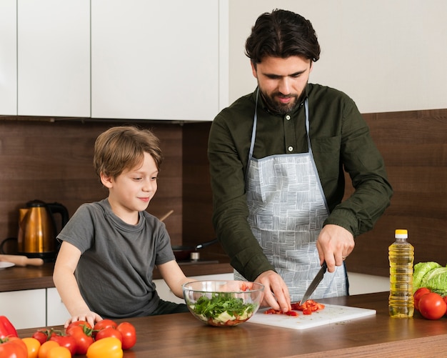 Ángulos altos hijo y padre cocinando ensalada