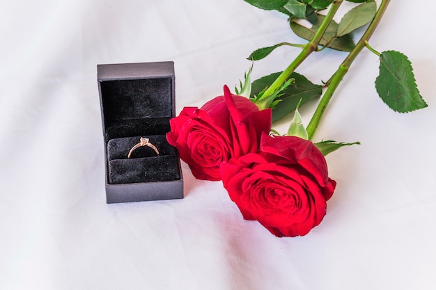 Anillo de boda con rosas rojas en mesa blanca.