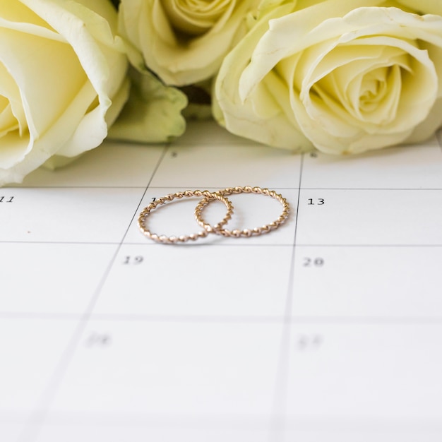 Anillos de boda en fecha calendario con rosas amarillas.