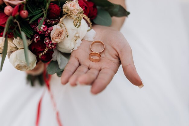 Anillos de boda en la mano de la mujer, ramo de flores rojas y blancas, detalles de boda