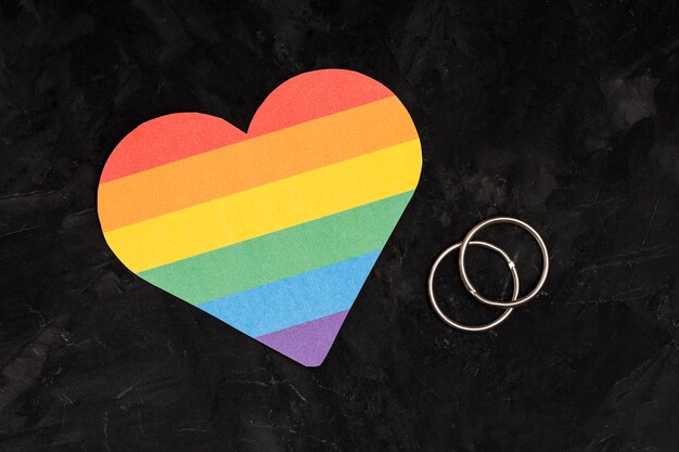 Anillos de boda multicolores y corazón LGBT sobre fondo negro