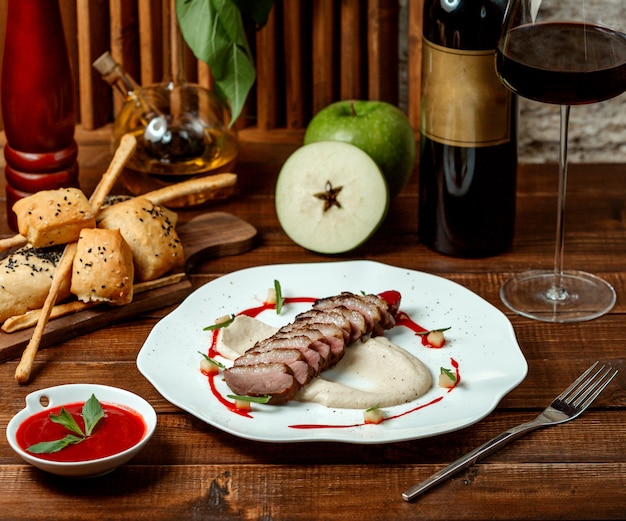 Anillos de carne con puré de manzana y una copa de vino tinto.