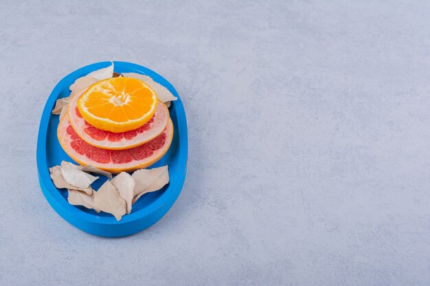 Anillos frescos de pomelo, limón y naranja en placa azul.