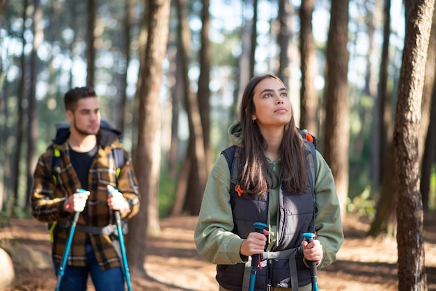 Animado par de jóvenes excursionistas. Hombre caucásico borroso con barba y mujer bonita con cabello oscuro con mochilas grandes caminando en el bosque. Hobby, naturaleza, concepto de amor.