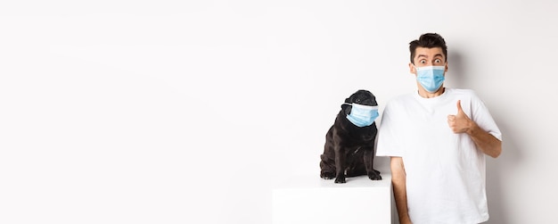Animales covid y concepto de cuarentena imagen de un joven divertido y un perro pequeño con máscaras médicas propietario s